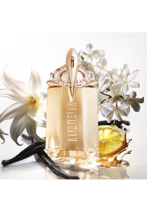 Flacon de parfum doré avec un capuchon multifacette, entouré de fleurs blanches, de gousses de vanille et de tranches de citron, reflétant la lumière sur une surface lisse.