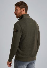 Sudadera de color verde oliva con un cuello alto, textura acanalada y un parche negro de la marca en la manga izquierda.