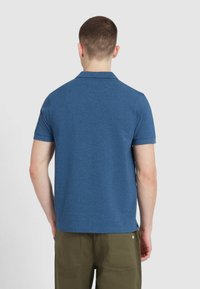 Niebieska koszulka polo z krótkim rękawem i kołnierzykiem, wykonana z teksturowanej tkaniny. Widok z tyłu pokazuje prosty krój i minimalne detale wzornicze.