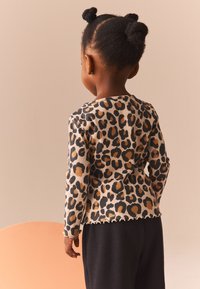 Leopard-print long-sleeve top made of ribbed fabric, featuring a scalloped hemline and black and brown patterns, paired with dark pants.