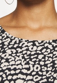 Tissu noir et crème à motif abstrait d'animaux avec un grand col, une texture lisse et des détails de couture visibles.