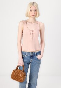 Light pink ribbed tank top with a scoop neckline, adorned with a bow and buttons, paired with blue jeans and a brown quilted handbag.