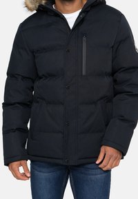 Dunjakke i marineblå med pelsforet hætte, forreste lynlås, knaplukning og to sidelommer. Tekstureret quiltet design.