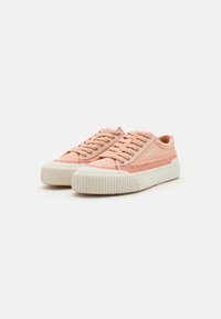 Light pink canvas sneakers with white rubber soles, round laces, and textured side accents, featuring a subtle logo detail.