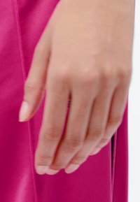Hand with natural nails resting against bright pink fabric with visible seam detail.