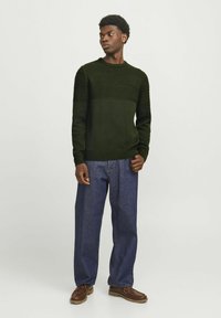 Pull vert foncé avec des rayures horizontales texturées, col rond, poignets côtelés, associé à un pantalon en denim bleu et des chaussures bateau marron.