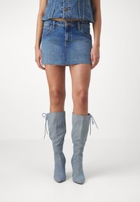 Jupe en denim mini avec ourlet effiloché associée à des bottes en denim montantes. Les deux articles sont de couleur bleu clair, mettant en valeur une texture denim cohérente.