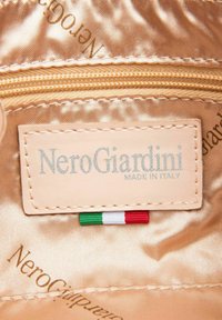 Etichetta NeroGiardini in pelle beige, testo impresso, con la dicitura "MADE IN ITALY", e un piccolo accento della bandiera italiana sottostante su fodera in raso.