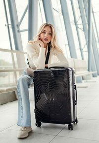 Černý tvrdý kufr s vlnkovým vzorem, čtyřmi kolečky a sklopnou rukojetí. Rozměry nejsou specifikovány.
