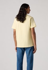 Tricou din bumbac galben, cu mâneci scurte, guler rotund și o croială lejeră, purtat cu blugi din denim albastru. Design simplu, cu o culoare uniformă.