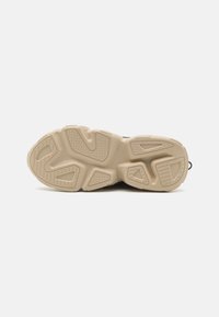 Suela de goma beige con patrones de banda de rodadura geométricos, ligeramente curvada, mostrando un diseño resistente al desgaste en una zapatilla deportiva.