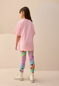 Rosa übergroßes T-Shirt kombiniert mit bunten Leggings, die Tiergesichter aus Cartoons zeigen. Das Outfit wird durch weiße High-Top-Sneaker ergänzt.
