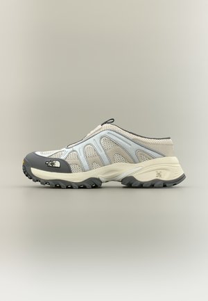 Μπεζ, γκρι και λευκό πεζοπορικό παπούτσι χωρίς κορδόνια με πλέγμα και λαστιχένια σόλα, με τη μάρκα "The North Face" στο μπροστινό μέρος, πλευρική όψη.