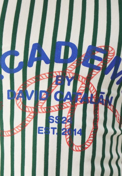 Grønn og hvit stripete stoff med blå tekst "ACADEM" og rødt tau-design, med "BY DAVID CATALÁN" i midten. Størrelsesmarkeringer til stede.
