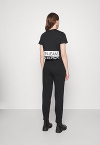 Svart bomullströja och matchande joggers. T-shirten har en vit "Calvin Klein Jeans" logotyp över ryggen. Slim-fit design med mjuk textur.