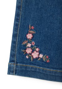 Tejido de mezclilla azul oscuro con bordado floral en tonos de rosa y verde en el dobladillo, con detalles de costura visibles.