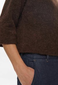 Rjav, puhast pletenina pulover s skrajšanim dizajnom in širokimi rokavi, v kombinaciji s temno modrimi kavbojkami z sprednjim žepom.