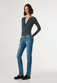 Bodysuit rayé bleu marine à manches longues avec un décolleté en V profond, associé à un jean droit bleu clair et des chaussures noires avec des accents argentés.