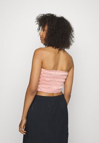 Top cropped em rosa claro, sem alças e com franzido, apresentando um tecido elástico e texturizado. Combinado com uma saia escura e fluida para contraste.