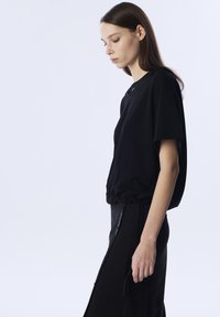 Zwarte T-shirt met korte mouwen en een relaxte pasvorm, voorzien van een trekkoord in de taille, minimale ontwerp elementen en een zachte textuur.