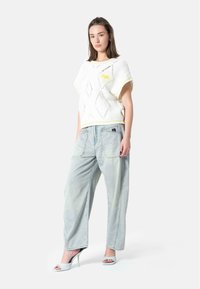 Hvit strikket kortermet genser med diamantmønster og gul kant, kombinert med lyseblå vid jeans og åpne hæler.