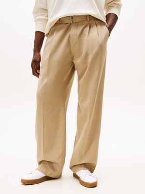 Beige plisserede bukser lavet af letvægtsstof, med bælt, sidelommer og en løs pasform. Parret med hvide sneakers.