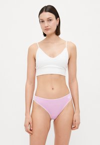Hvit bomullsbralette med tynne stropper, paret med lys rosa bikini-briefs med hvit logo, glatt tekstur og enkelt design.