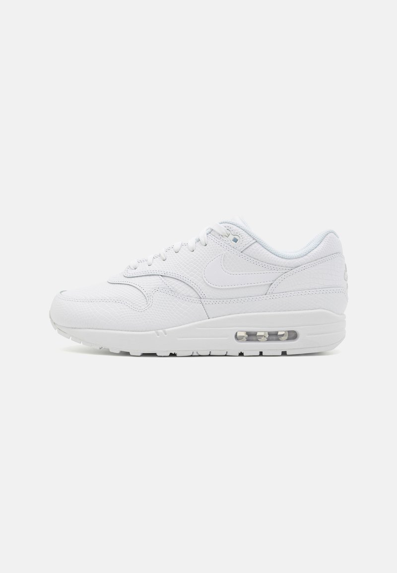 Ténis Nike Air Max 1 brancos, com um upper de couro texturizado, fecho de atacadores e amortecimento de ar visível na sola.