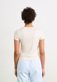 Lichtbeige, shirt met korte mouwen van een zachte, gladde stof. Heeft een ronde halslijn en een strak ontwerp aan de achterkant.