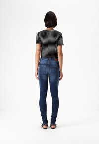 Črna in bela črtasta kratka majica, združena s temno modrimi oprijetimi kavbojkami, ki prikazujejo zadnje žepe in usnjeno oznako na pasu.