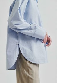 Cămașă button-up de culoare albastru deschis, confecționată din bumbac, cu un tiv rotunjit și fante laterale, cu mâneci lungi și croială relaxată. Asortată cu pantaloni striped.