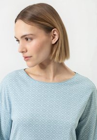 Haut bleu clair avec un motif géométrique blanc, col rond et coupe ample. Manches longues avec une texture douce, conçu pour le confort et la respirabilité.