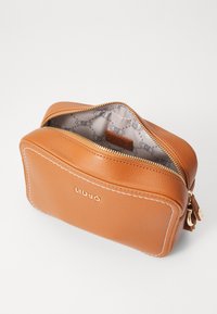 Braune Leder-Kosmetiktasche mit einem Reißverschluss, weißer Nahtdetail und einem gemusterten, beigen Innenraum mit Logodruck.