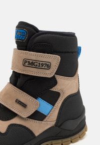 Pruunid ja mustad pahkluu saapad tekstuurse pealmise osaga, siniste aktsentide, Velcro rihmade ja Go-Tex sildiga. Omab tugevat tallat, mis tagab haarduvuse.
