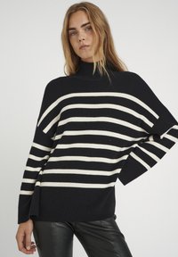 Übergroßer schwarz-weißer gestreifter Pullover mit hohem Stehkragen, breiten Ärmeln und lässiger Passform. Strickstoff mit weicher Textur.