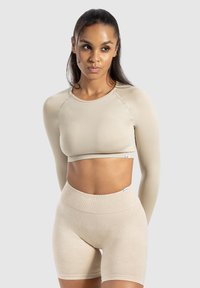 Top court beige clair à manches longues et texture côtelée, associé à un short taille haute assorti, avec des accents de branding minimalistes.