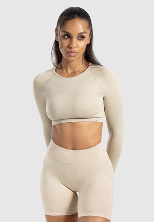 Lichtbeige crop top met lange mouwen en ribbelstructuur, gecombineerd met bijpassende high-waisted shorts, met minimale merkaccenten.
