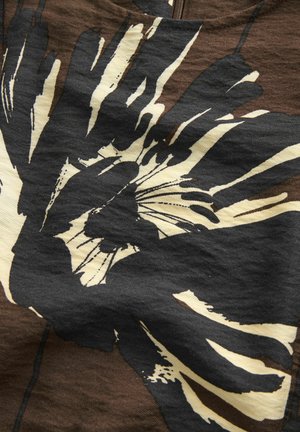 Fette grafische Darstellung von sich überlappenden schwarzen und cremefarbenen Handabdrücken auf einem strukturierten braunen Stoffhintergrund, die einen auffälligen visuellen Kontrast schaffen.