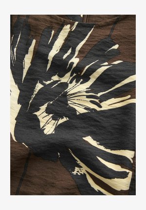 Odvažan grafički dizajn preklapanja crnih i krem rukotisaka na teksturiranoj smeđoj tkanini, stvarajući upečatljiv vizualni kontrast.