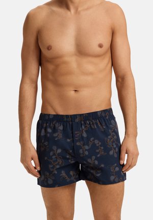 Marineblaue Badeshorts mit einem Blumenmuster in Brauntönen, ausgestattet mit einem elastischen Bund und einem lockeren Schnitt, aus leichtem Stoff gefertigt.