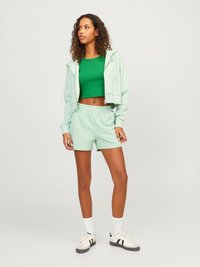 Mint zeleno kratek hoodie in ujemajoče se kratke hlače, ki vključujejo prilegajoč zgornji del v zeleni barvi. Obleka vključuje bele nogavice in dvoslojne športne copate.