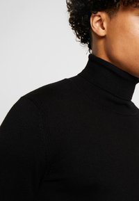 Maglione a collo alto nero in tessuto a costine, con un design aderente e dettagli delle spalle senza cuciture.