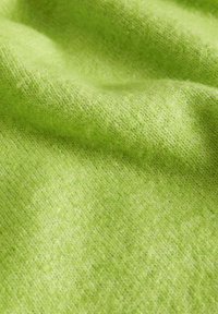Weicher, strukturierter Stoff in leuchtendem Grün mit einem glatten Glanz und subtilen Farbvariationen, der ein gestricktes Muster aufweist.