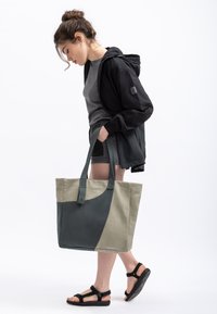 Tote bag gemaakt van duurzaam materiaal, met een bicolor ontwerp in donkergroen en beige, twee stevige handvatten en een minimalistische sluiting.