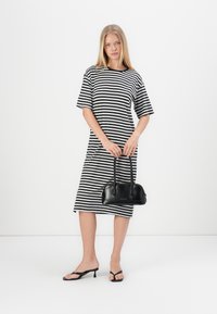 Stripet svart og hvit midi-kjole med korte ermer, parret med en liten svart håndveske og svarte flate sandaler. Glatt stoff, avslappet passform.