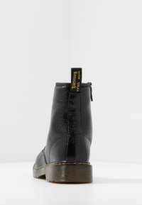 Schwarzer Knöchelstiefel aus strukturiertem Leder, mit gelber Naht und Schlaufe zum Anziehen. Verfügt über eine flache Gummisohle und eine schlanke, stromlinienförmige Silhouette.