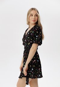 Vestido negro con patrones celestiales multicolores, con mangas cortas abullonadas, escote en forma de v y detalle de cintura atada.