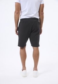 Sorte teksturerede shorts med elastisk talje og sidelommer. Båret med en hvid t-shirt og hvide sneakers, set fra ryggen.