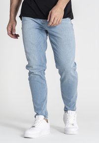 Vaqueros de denim azul claro con un corte slim, que presentan un diseño clásico y un ligero desvanecimiento, combinados con zapatillas blancas.