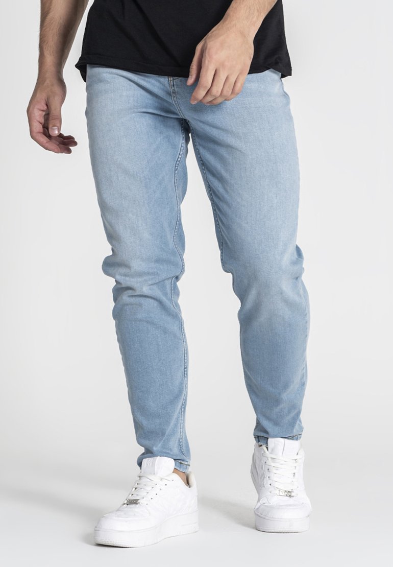 Vaqueros de denim azul claro con un corte slim, que presentan un diseño clásico y un ligero desvanecimiento, combinados con zapatillas blancas.